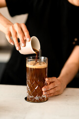 Female barista pouring coffee on ice cubess in high old fashioned glass with tonic served on table...