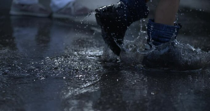 Close-up rainboots walking through water puddles splashing droplets everywhere at high-speed 800 fps during rainy afternoon evening