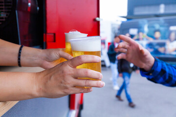 Zwei Hände reichen einer Person Bier in Plastikbechern
