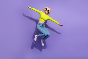 Full length photo of cheerful glad girl wear trendy clothes have fun fly air empty space isolated on purple color background