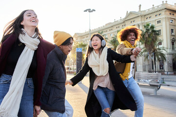 Group of young friends have fun together walking excitedly in open air. Multiracial people holding...