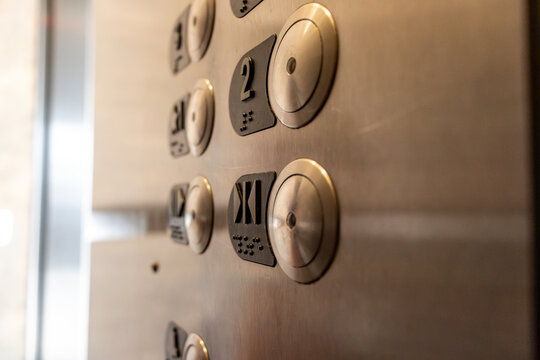 A close-up of an elevator control panel - stainless steel with round buttons - numbers and braille - emergency call and door open buttons. Taken in Toronto, Canada.