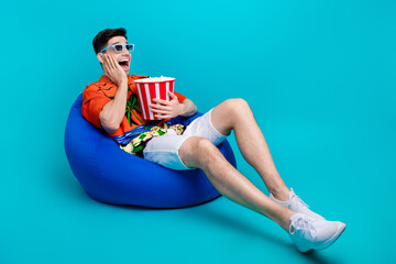 Full size photo of ecstatic man dressed print shirt hold popcorn in lay on pouf staring empty space...