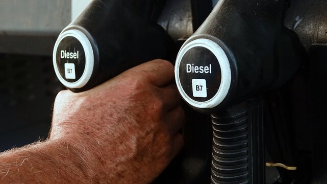 Close-up of a hand holding a diesel fuel nozzle at a gas station pump, ready to refuel a vehicle at a service station