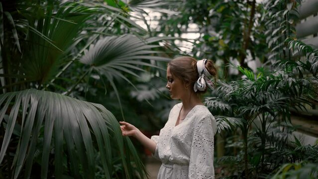 Romantic young woman strolling botanic garden and touching palm leafs