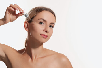 Naklejka premium Beautiful woman applying cosmetic serum onto her face on white background, space for text