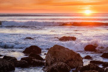 Atlantic ocean sunset with waves and rocks at Costa da Caparica, Portugal