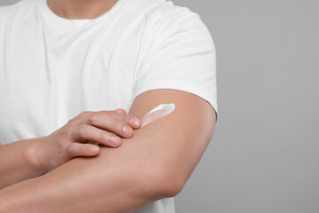 Man applying body cream onto his arm on light grey background, closeup. Space for text