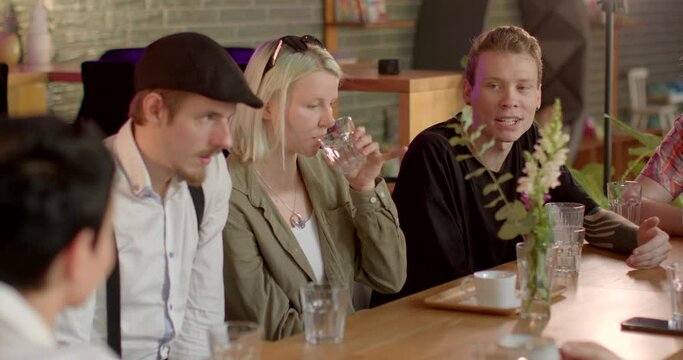A group of people expressing an oral opinion at a table. The guy wearing glasses speaks the information with inspiration. Motivation communication energy up. Flowers on the table.