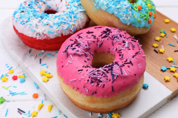 Sweet glazed donuts decorated with sprinkles on white table, closeup. Tasty confectionery