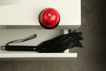 Red bell and black whip in drawer indoors, selective focus. Sex toys