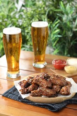 Tasty roasted chicken wings served with beer on wooden table