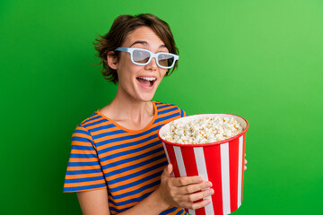 Photo portrait of attractive young woman hold popcorn bucket eating wear trendy striped clothes isolated on green color background