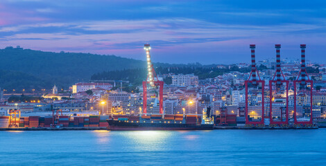 View of Lisbon port with moored sea container ship with port cranes in the evening twilight over Tagus river. Lisbon, Portugal
