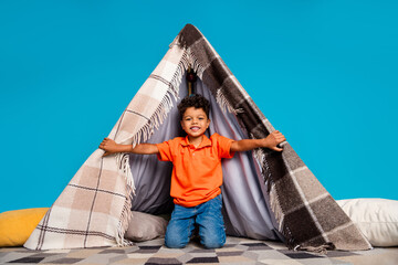 Photo of sweet adorable kid boy playing in homemade tent wigwam isolated over blue color background © deagreez