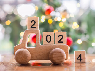 Wooden block number 2024 on wooden toy car with Christmas light bokeh background. Merry Christmas and Happy New Year, The concept of car in new year 2024.