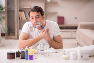 Young man shaving face at home