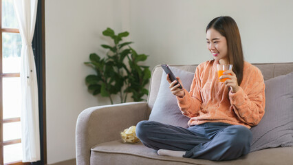 Women drinking orange juice and using smartphone to watching entertainment in lifestyle at home