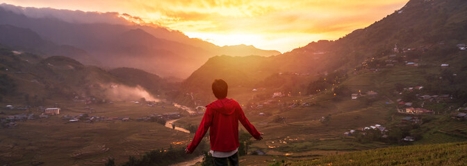 Young man traveler looking at beautiful landscape with mountains and green rice terraces view at sunset in Sapa, Vietnam