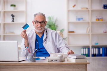 Old male doctor holding credit card