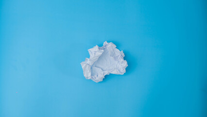 A paper ball is spread out into a blank sheet on blue background. Crumpled blank white paper with copy space for text or advertising space.