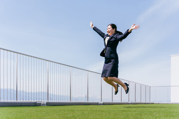 会社の屋上でジャンプする笑顔のビジネスウーマン（チャレンジ・スキルアップ・就職活動・昇進）

