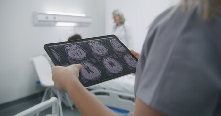 Mature medic speaks with African American teenager. Patient lies on bed in hospital ward. Female doctor learns MRI or CT scan results on digital tablet computer. Medical staff at work in modern clinic