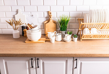 A set of stylish kitchen utensils plates, bowls, cutting boards, spoons on a wooden countertop opposite a white brick wall.