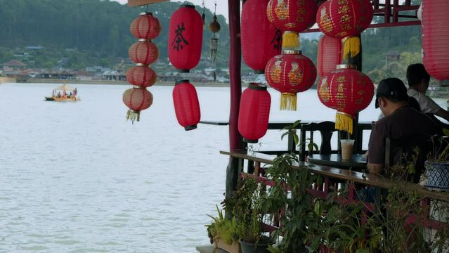Asian man enjoys the view of the lake with red chinese lanterns.