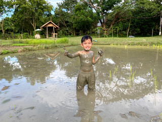 Thailand Asia boy is enjoy playing in the mud of rice field. Outdoor kid learning activity.