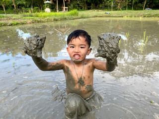 Thailand Asia boy is enjoy playing in the mud of rice field. Outdoor kid learning activity.