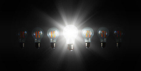 An illuminated or glowing  lightbulb among other unlit bulbs on dark background represents new...