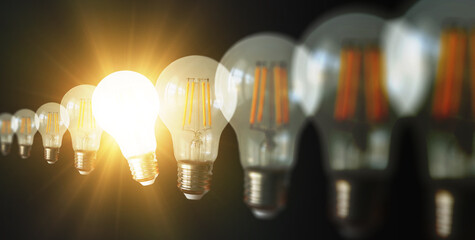 An illuminated or glowing lightbulb among other unlit bulbs on a dark background represents new ideas, innovation, creativity, understanding, knowledge, and inspiration.