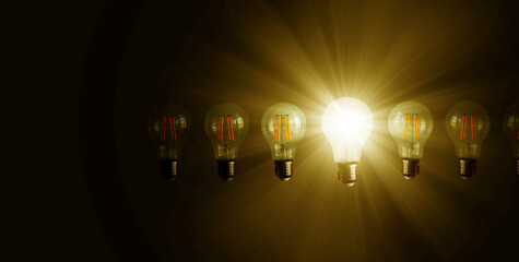 An illuminated or glowing  lightbulb among other unlit bulbs on dark background represents new...