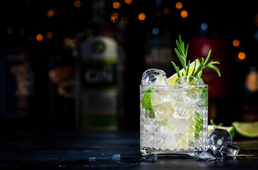 Gin fizz cocktail drink with dry gin, lime juice, sugar syrup, soda, fresh rosemary and ice. Black bar counter background, steel bar tools and bottles
