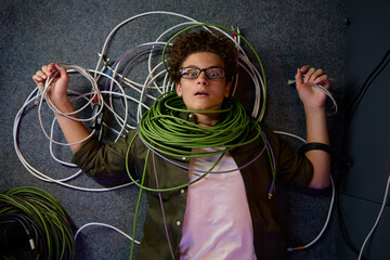 Frustrated overwhelmed teenager IT engineer lying on floor wrapped in wire