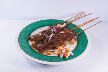 Madura chicken satay. Chicken satay with peanut sauce and a sprinkling of sliced red onion and chili. On a green plate.