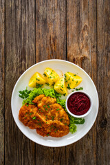 Crispy breaded seared chicken cutlet with boiled potatoes and beets on wooden table
