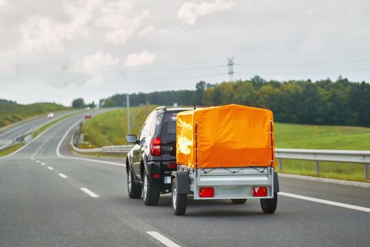 SUV with trailer goes on the highway. Moving stuff with a small rentable trailer.