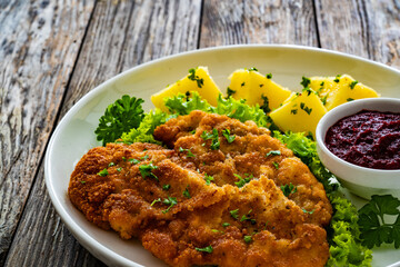 Crispy breaded seared chicken cutlet with boiled potatoes and beets on wooden table
