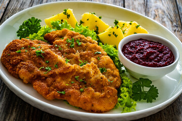Crispy breaded seared chicken cutlet with boiled potatoes and beets on wooden table
