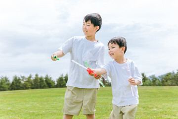 草原・公園でシャボン玉スティックで遊ぶ少年・兄弟・子供
