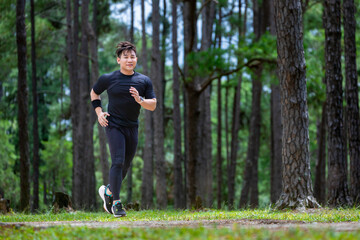 Asian trail runner is running outdoor in the pine forest dirt road for exercise and workout...