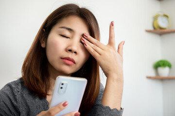 Asian woman suffering from eye pain from phone screen time cause of blue light