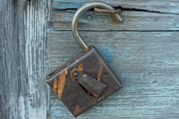 one open rusty iron retro brown reliable secure padlock without key hanging on an iron shackle on a wooden gray old door on the street during the day