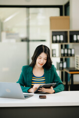 Fototapeta premium Beautiful Asian woman using laptop and tablet while sitting at her working place. Concentrated at work. in office..