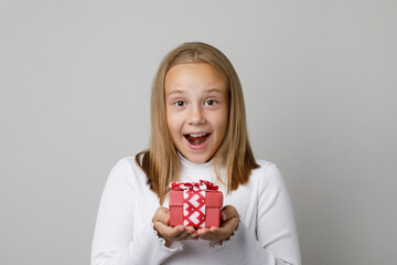 Portrait of happy surprised little child girl holding gift present box on white studio wall background. Cute excited kid