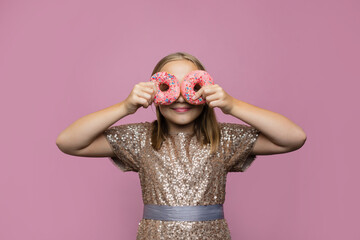Beautiful young girl holding two donut on pink wall background. Child having fun with doughnut....