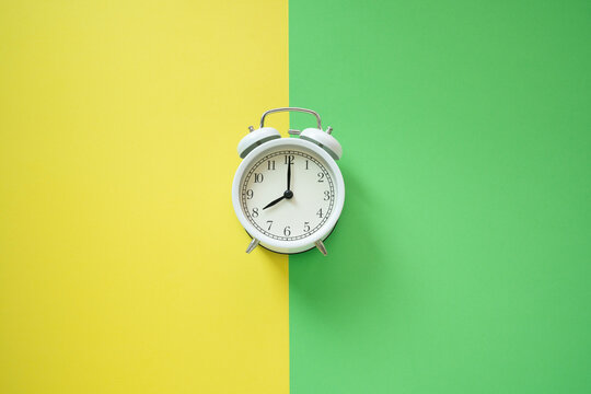 White retro alarm clock on yellow and green table background, vintage style, flat lay
