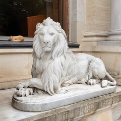 White marble statue of a lion sitting in front of Ottoman Beylerbeyi Palace, with sleeping cat in...